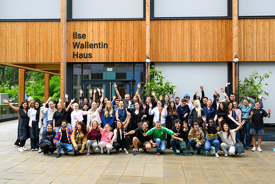 Group of people posing happily in front of Ilse Wallentin Haus, an atrium-like building with large wooden panels.